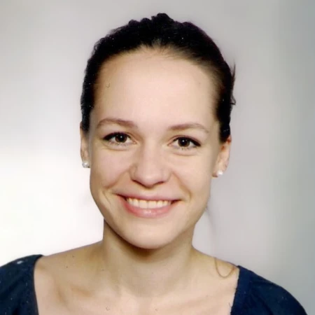 A young woman with dark hair and a wide, friendly smile. She is wearing pearl earrings and a dark navy top.