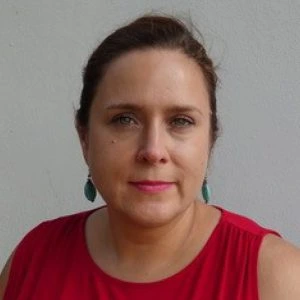 Headshot of Petra Guasti with her brown hair pulled back, looking directly at the camera. She wears a red top and turquoise teardrop earrings.