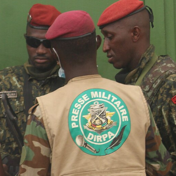 Three men in red berets and camouflage uniforms. One wears a beige vest with 