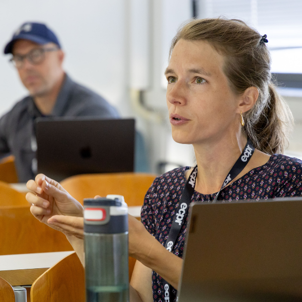 A woman in the audience at an ECPR conference, sitting at a desk with a laptop and water bottle in front of her