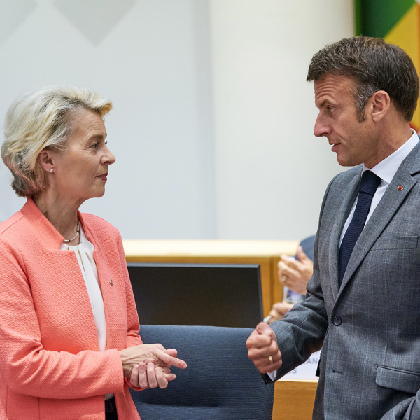 Ursula von der Leyen wears a peach coloured jacket and talks to Emmanuel Macron, who wears a grey suit