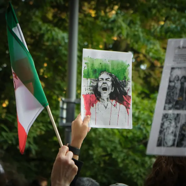 Protestor holds a drawing of a screaming woman with Iranian flag colours, alongside a waving Iranian flag.
