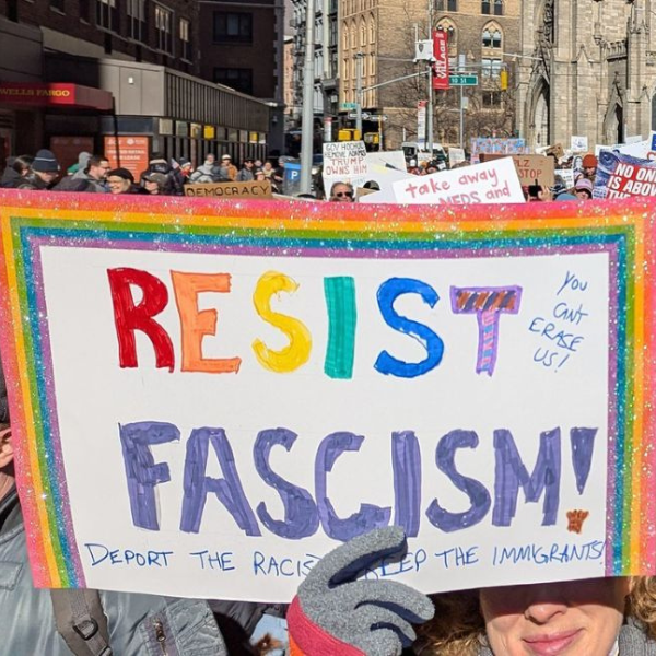 A crowd of demonstrators on a street. One of them holds a sign that says 