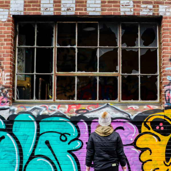 A person looks at a wall covered in graffiti and a broken window