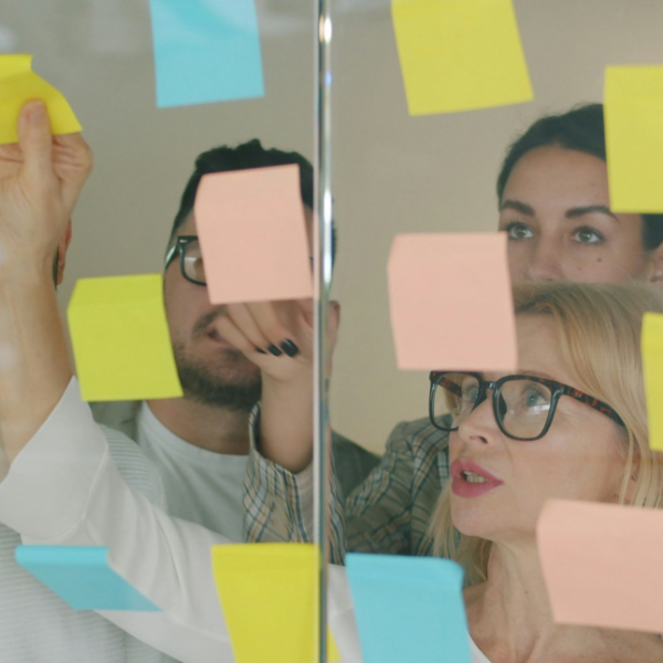 A group of people look at coloured post-it notes on a glass wall.