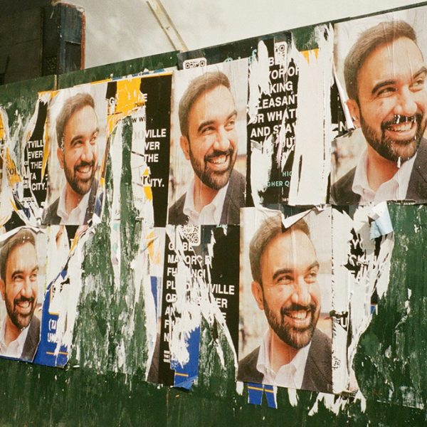 Posters of Zohran Mamdani on a board.  Some of the posters have been ripped.
