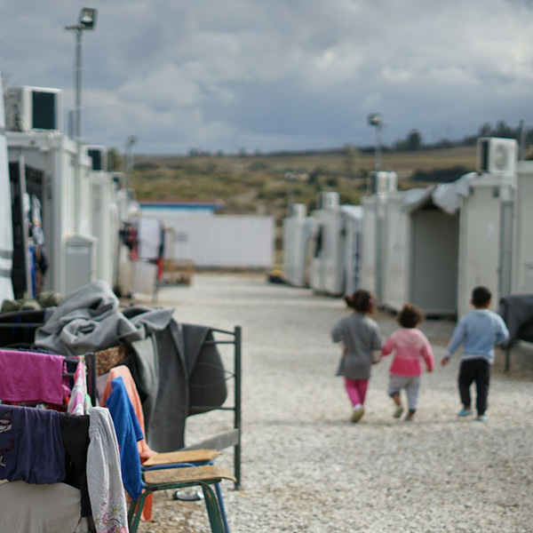 Three small children, seen from the rear, walk through a refugee camp in northern Europe